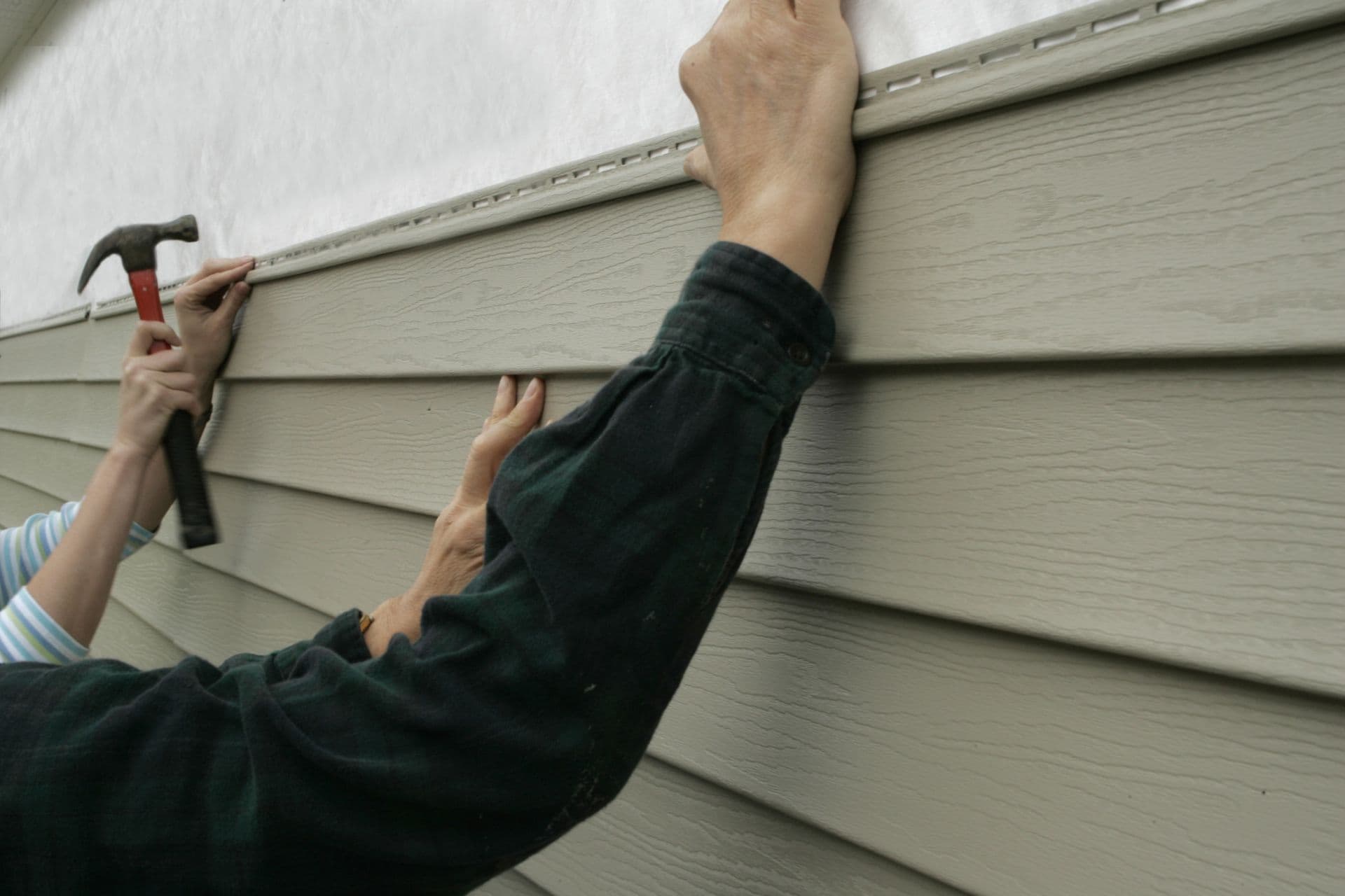 Workers install tan siding on a house.