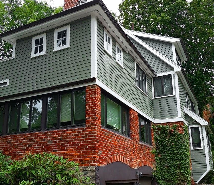 A house with red brick first floor and sage green vinyl siding on the second floor.